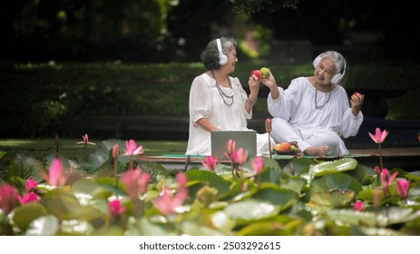 Two elderly women enjoying a nature setting listen music ,eating fresh focusing a plant lotus in the greenery around them is elder lifestyle concept. - Powered by Shutterstock