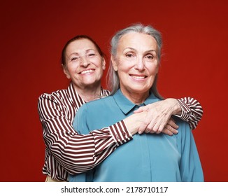 Two Elderly Women Friends Hugging On Red Background. Lifestyle And Old People Concept.