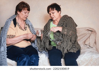 Two Elderly Women Friends And Neighbors Look After Each Other. One Woman Pours Another From A Decanter Into A Glass Of Water, Drink The Medicine At Home