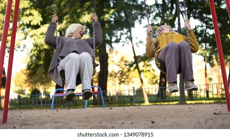 Two Elderly Women Laughing Riding Swings In Park, Elderly Friends, Retirement