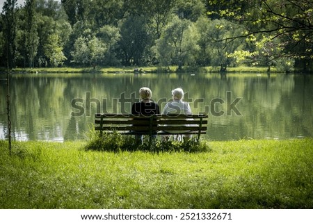 Two elderly women sit by the lake and admire the nature, pensioners