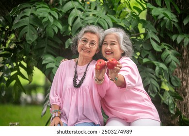 Two elderly women are sitting outdoors and  they eating apple fresh fruit and orange juice is time to relaxed with good healthy of elderly on holiday lifestyle concept. - Powered by Shutterstock