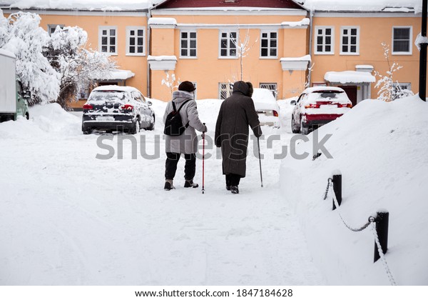 Two elderly\
women walk along the snow-covered alley of the winter Park. Rear\
view. Healthy lifestyle of\
pensioners.