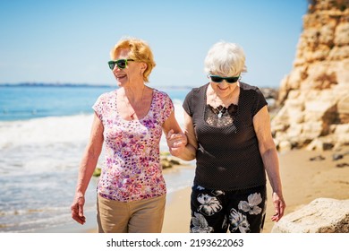 Two Elderly Women Are Walking Along The Rocky Shore, Talking And Laughing, Having A Pleasant Time Together