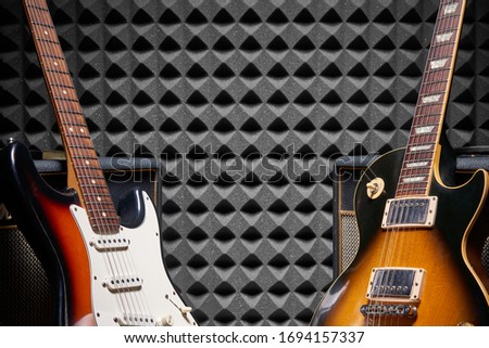Two electric guitars leaning on Guitar Amplifier Combo over acoustic foam panel background, with copy space between