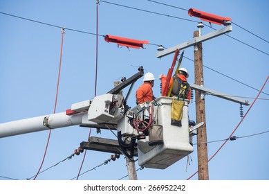 Two electric power workers hover in a bucket as they make repairs.