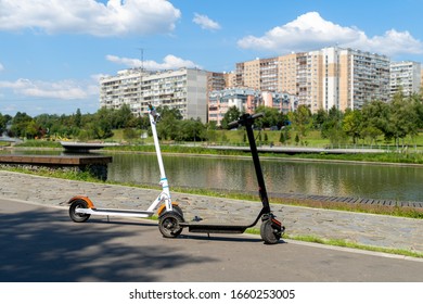 Two electric scooters, white and black, stand on the bandwagon on the street. Sunny summer day. Modern city transport. City park near the river. - Shutterstock ID 1660253005