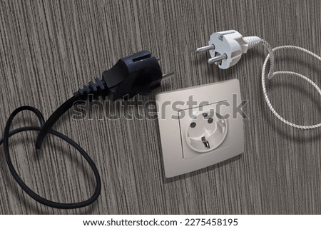 Two electrical plugs, in the background, wall with an electrical outlet.