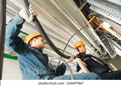 two electrician builder engineers workers installing industrial cable into fuse box
