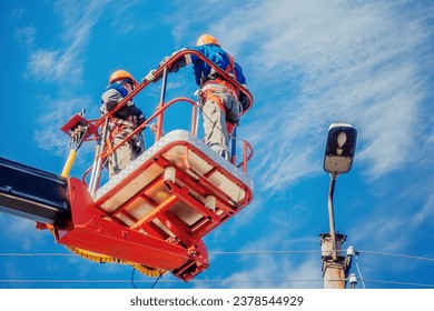 Two electricians from cradle of aerial platform or crane are repairing street lighting lamp. Professional electricians wearing helmets, overalls and insurance work at heights. View of workers from - Shutterstock ID 2378544929