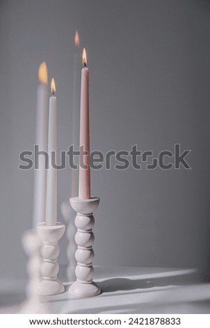 Two elegant bubble taper candle holders with taper candles in side blind lights on grey background. Interior design.
