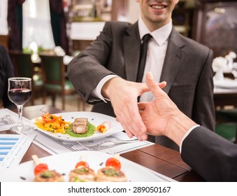 Two elegant business partners shaking hands while having business lunch. Great deal agreement.