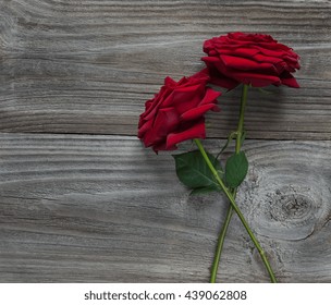 Two elegant red roses on a long stem with green leaves on old wooden background