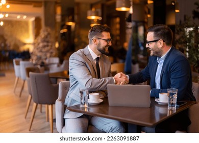 Two elegant stylish corporate leaders shaking hands after a successful business meeting in a restaurant in the evening. Proud business partners shaking hands while sitting at table in restaurant. - Shutterstock ID 2263091887
