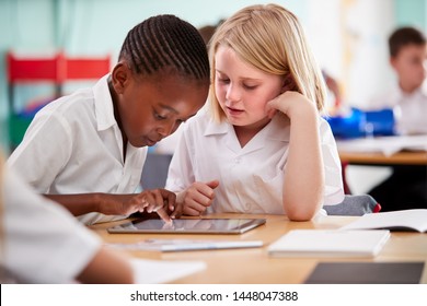 Two Elementary School Pupils Wearing Uniform Using Digital Tablet At Desk