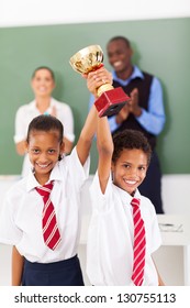 Two Elementary Students Holding A Trophy In Classroom