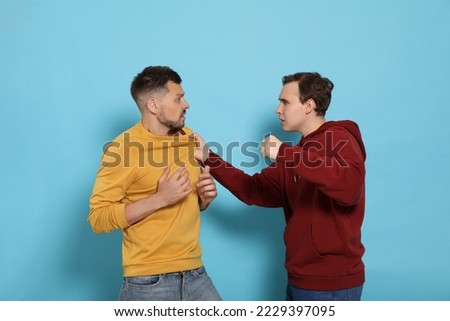 Two emotional men fighting on light blue background