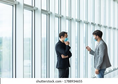 Two Employee Standing In Social Distance Wearing Face Mask Looking At Each Other And Talking In The Office.