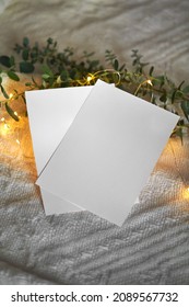 Two Empty 5x7 Tcard Mockup With Eucaliptus Leaves And Light Garland On A Knitted Beige Cozy Winter Background, Design Element For Invitation, Thank You Or Christmas Greeting Card.