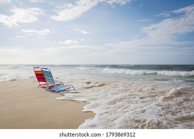 Two empty beach chairs facing the ocean and being overtaken by incoming tide