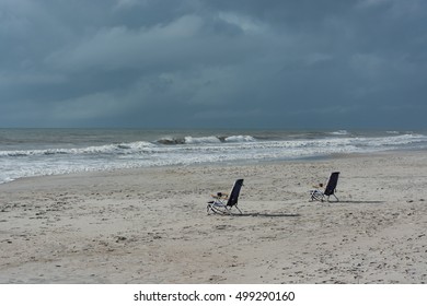 Two empty beach chairs sit at the edge of a stormy sea.  Loneliness.  Forgotten.  Waiting. 