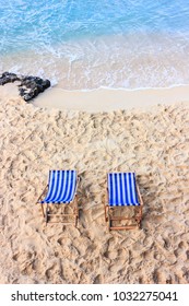 Two empty blue deck chairs on a sandy beach near the water