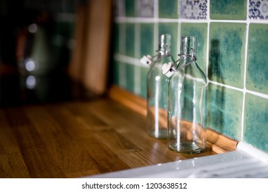 Two empty bottles stand on a wooden kitchen counter in a morning sunlight