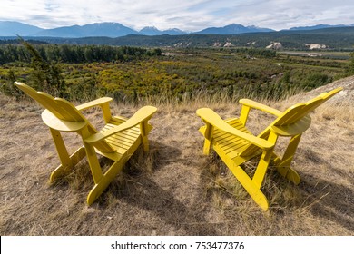 Two empty bright yellow adirondack chairs on a hillside over looking the Columbia Valley & Purcell Mountains in Radium Hot Springs, British Columbia, Canada during autumn