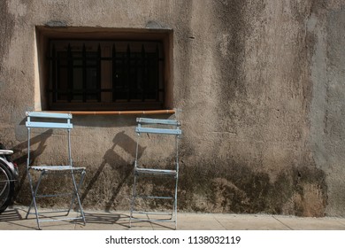 Two empty chairs on sidewalk in front of old buildings in France