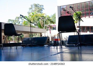 Two Empty Chairs On A Stage, With A Microphone In Front Of Them.