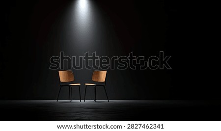Two empty chairs are positioned on a dark stage, bathed in the intense glow of a single spotlight from above.