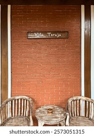 two empty chairs and an empty table made of wood placed in front of a red brick wall.