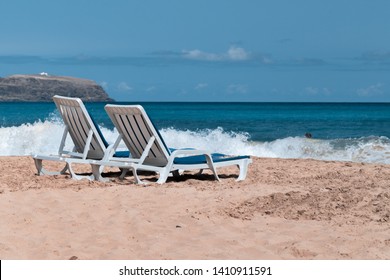 Two empty deck chairs on a deserted sandy beach on the ocean.