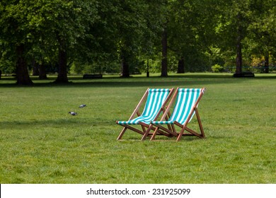 Two empty deck chairs with white and green stripes in the middle of a park