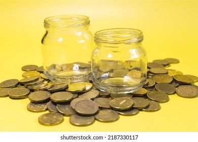 Two Empty Glass Jars On The Background Of A Scattering Of Coins Close-up Yellow Background.