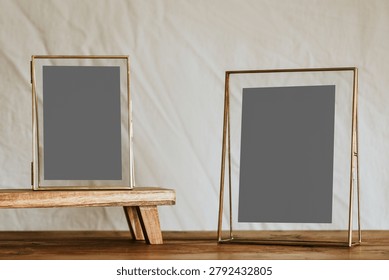 Two empty gold-framed photo frames on a wooden surface against a neutral background, one standing on a small wooden platform.