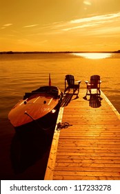 Two Empty Lounge Chairs On Dock With Anchored Vintage Motor Boat