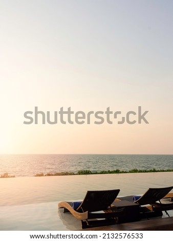 Two empty modern rattan sunbeds, bed chairs for guests on white marble floor at the pool in hotel resort on peaceful sunset sky background with copy space, holiday vacation concept, vertical style.