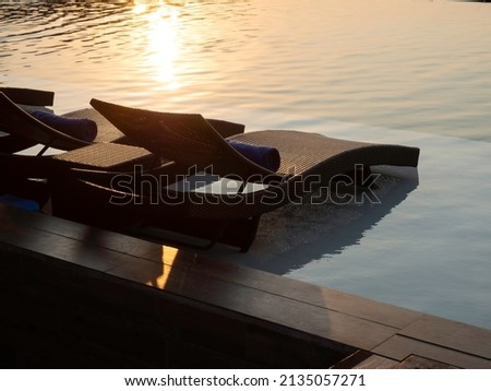 Two empty modern rattan sunbeds, bed chairs for guests on white marble floor at the pool in hotel resort on peaceful sunset sky background with copy space, holiday vacation concept.