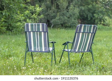 Two Empty Patio Chairs Standing In The Back Yard In The Garden On Green Lawn Grass. Patio Furniture. Family, Couple, Home, Love, Relax Concept 