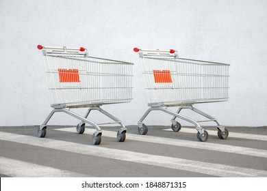 Two Empty Shopping Cart Trolley Stands near Mall with Copy Space. Grocery Cart on a White Wall Store Background. Couple Trolleys near Supermarket. E-commerce. Shopping Concept. Side View. Buy Online