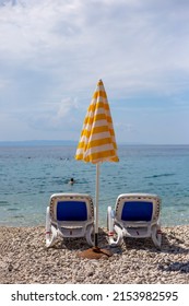 Two Empty Sun Loungers And Yellow Sun Umbrella Stand On The Beach