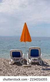 Two Empty Sun Loungers And Yellow Sun Umbrella Stand On The Beach