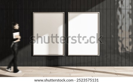 Two empty vertical posters on a black tiled wall, with a young woman holding a notepad walking by. Modern display, copy space concept