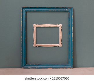 Two empty vintage picture frames, one painted blue, the other a smaller carved frame hanging on a teal colored wall for interior decor