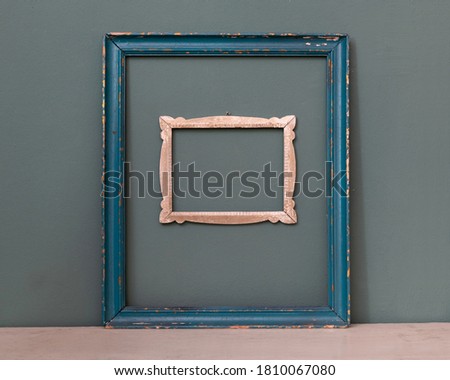 Two empty vintage picture frames, one painted blue, the other a smaller carved frame hanging on a teal colored wall for interior decor