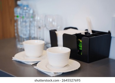 two empty white tea or coffee cups on a table in the hotel room. A set of dishes, kettle, coffee and tea for guests.
