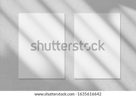 Two empty white vertical rectangle poster or business card mockups with diagonal window shadow on the gray concrete wall.Flat lay, top view. For advertising, brand design, stationery presentation.