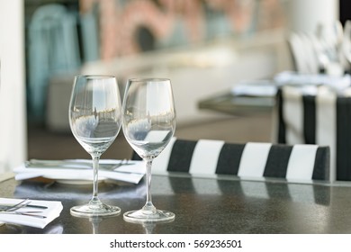 Two empty wine glasses arranged on a table in an open air restaurant or bar.