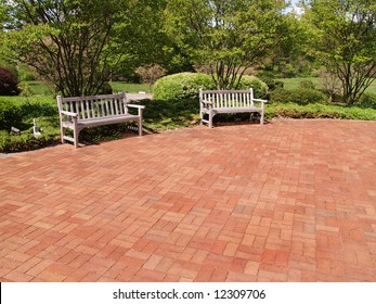 Two Empty Wood Benches By A Red Brick Patio In A Garden